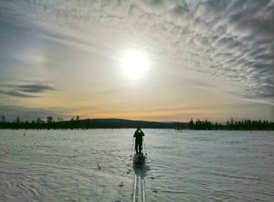 A skier heading towards the sun across a flat terrain.