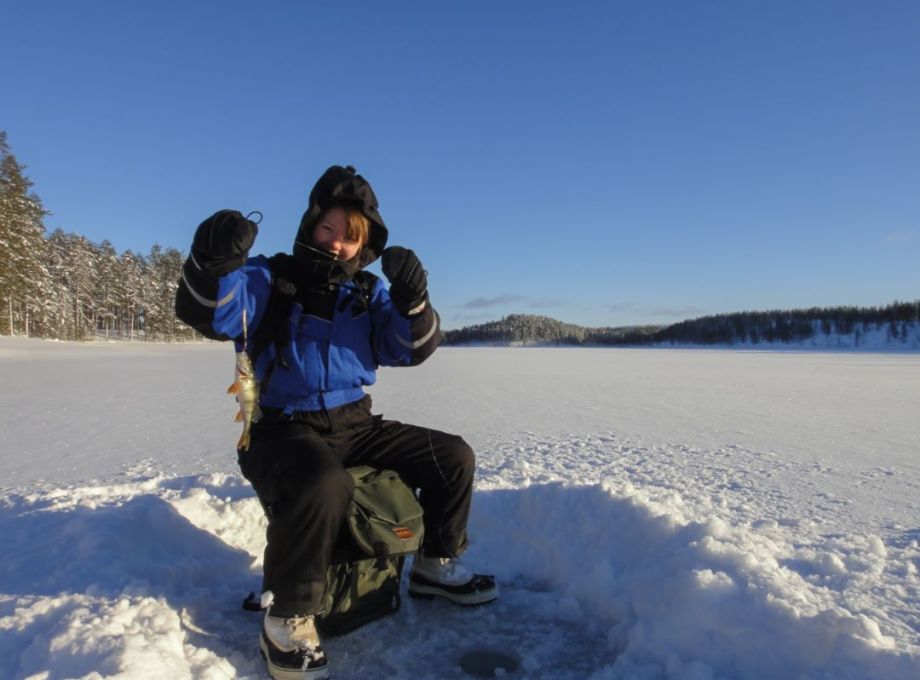 A girl ice-fishing and presenting her catch.