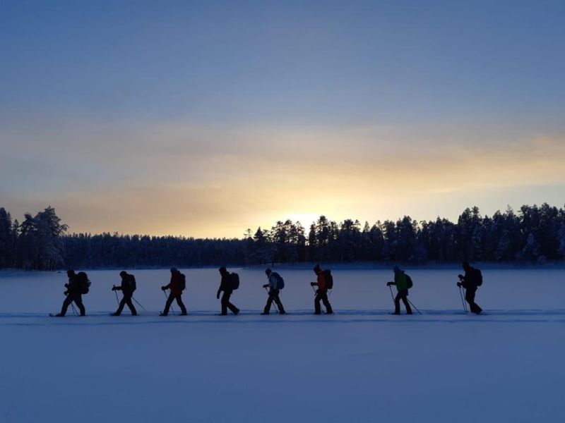 A group of snowshoers on a lake at sunset.