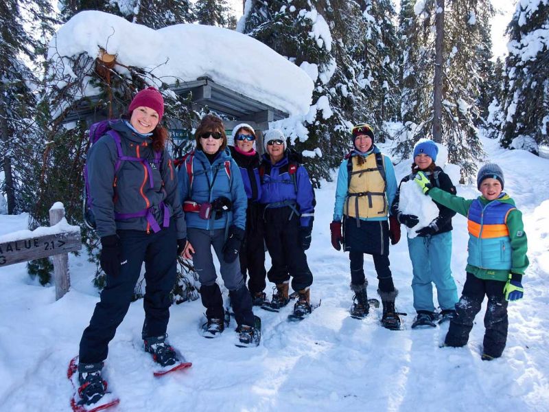 A group of adults and kids on snowshoes in the forest.