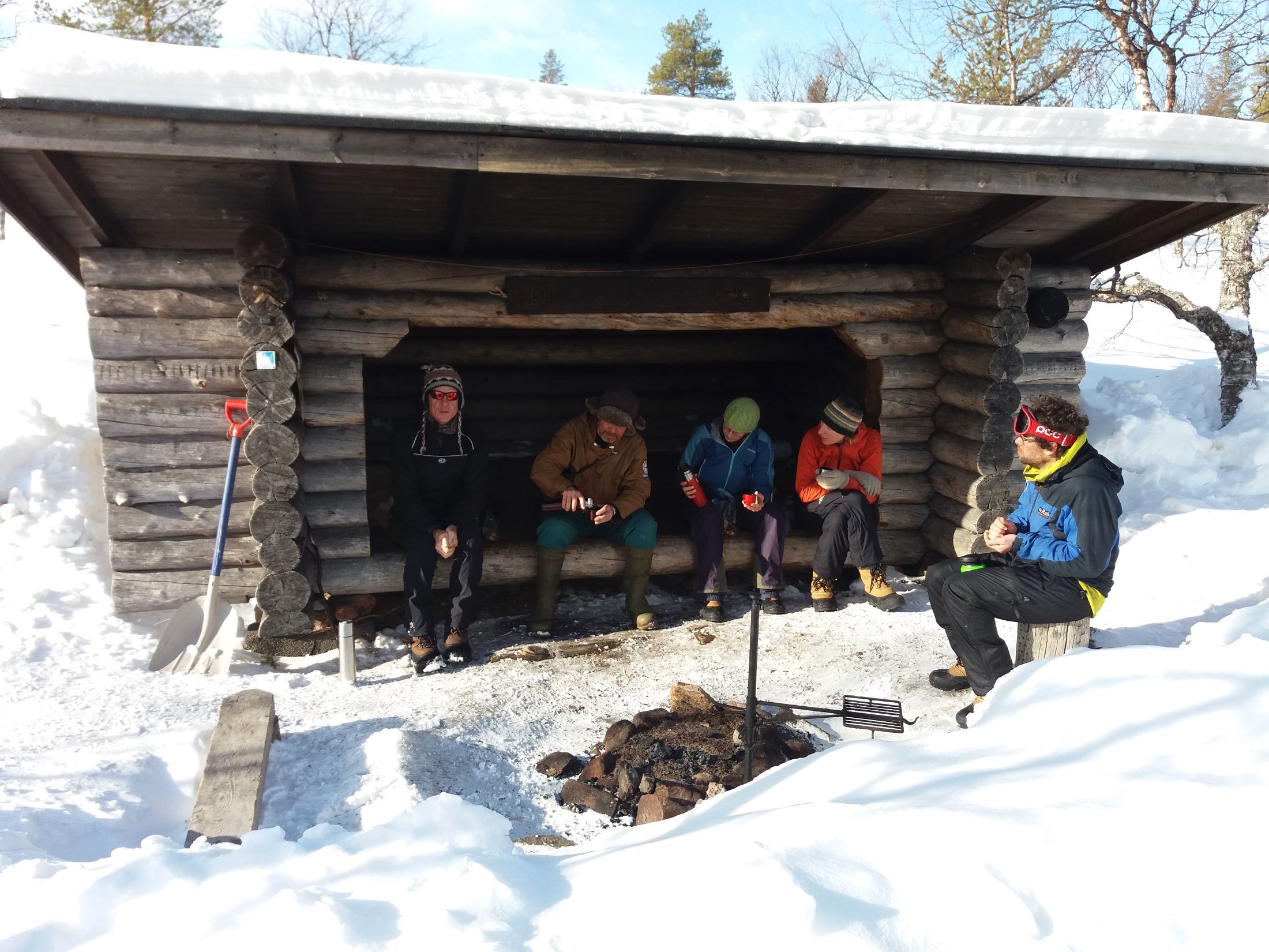 A group of skiers having lunch on a lean-to-shelter