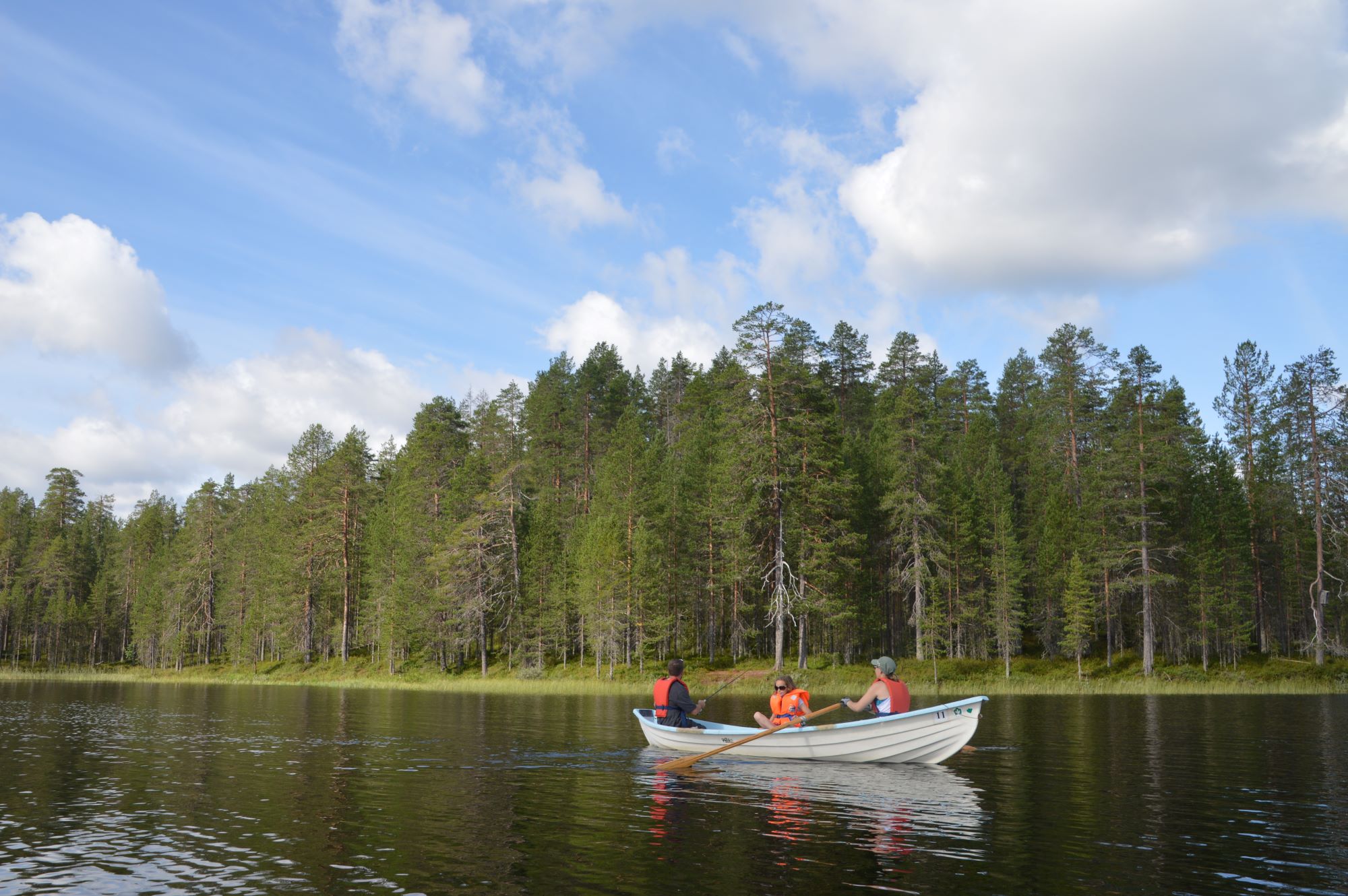 Three person on a rowing boat. It is a calm lake and sunny day.