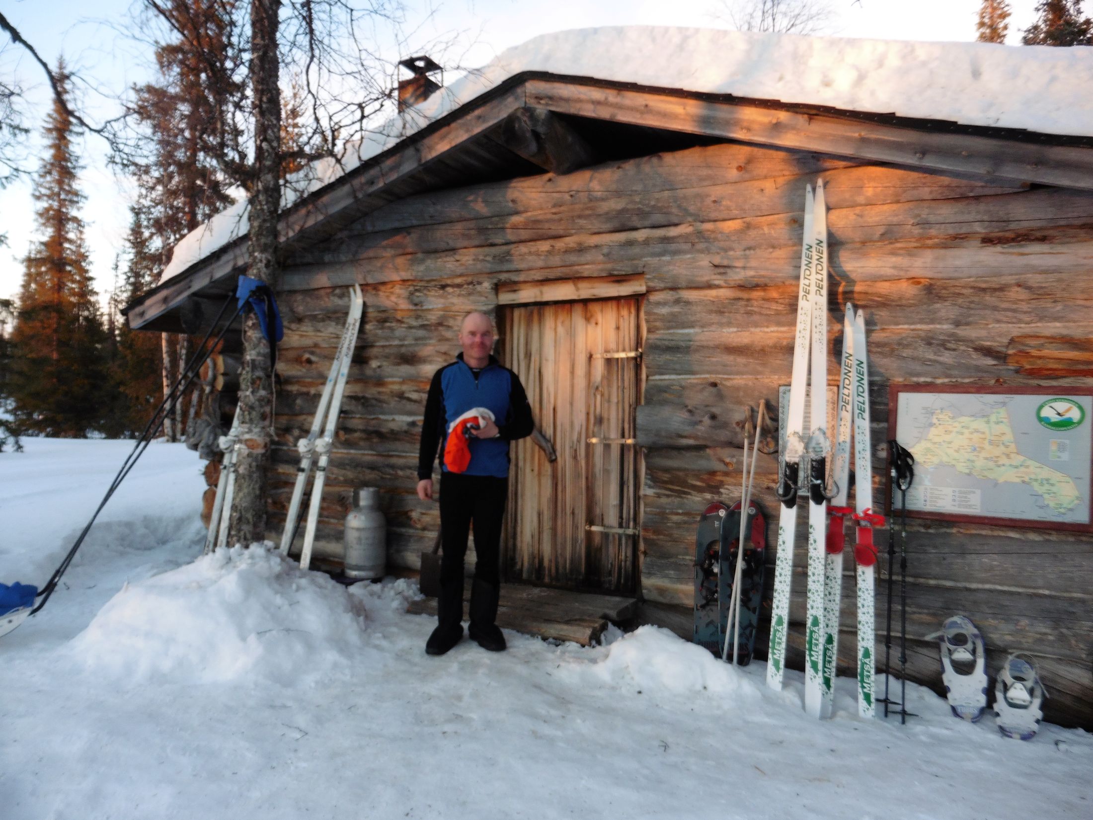 A man standing in front of a wilderness hut.