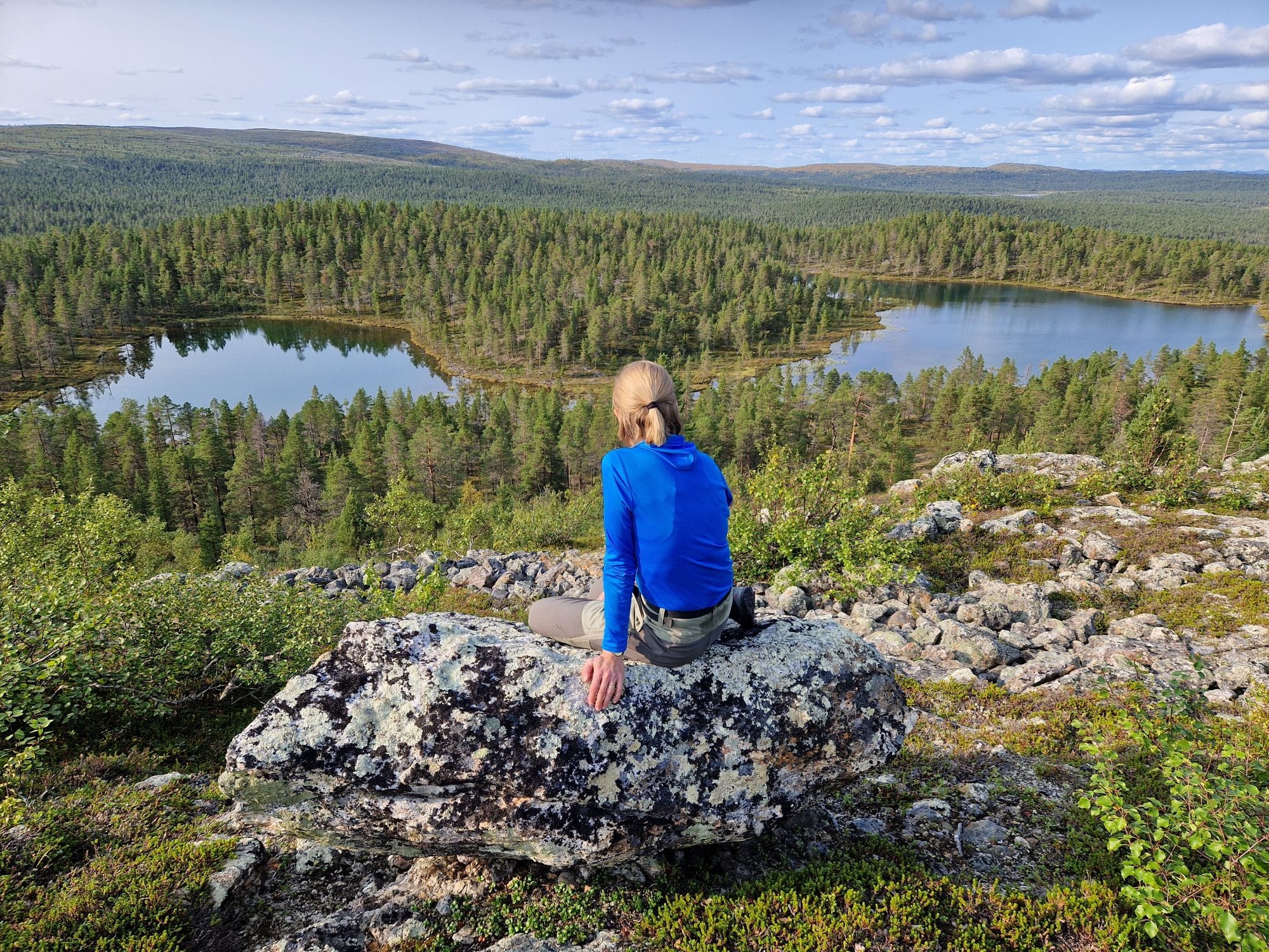 A woman sitting on a rock in a hill and looking over the open scenery
