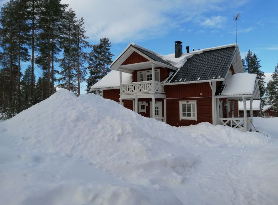 A red wooden house. A high pile of snow on the courtyard.